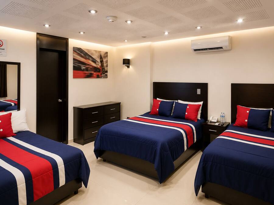 Une chambre d’hôtel avec trois lits, une table de chevet, un climatiseur fixé au mur et un tableau représentant un autobus rouge.