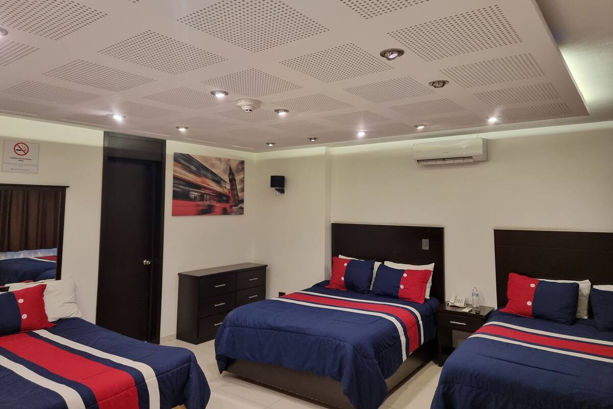 A hotel room with three beds, a large painting, a ceiling with recessed lighting, and an air conditioning unit.