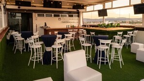 An indoor venue with white chairs and tables, a bar area, and a view through large windows. - Hotel Grand Elizabeth Durango (Durango)