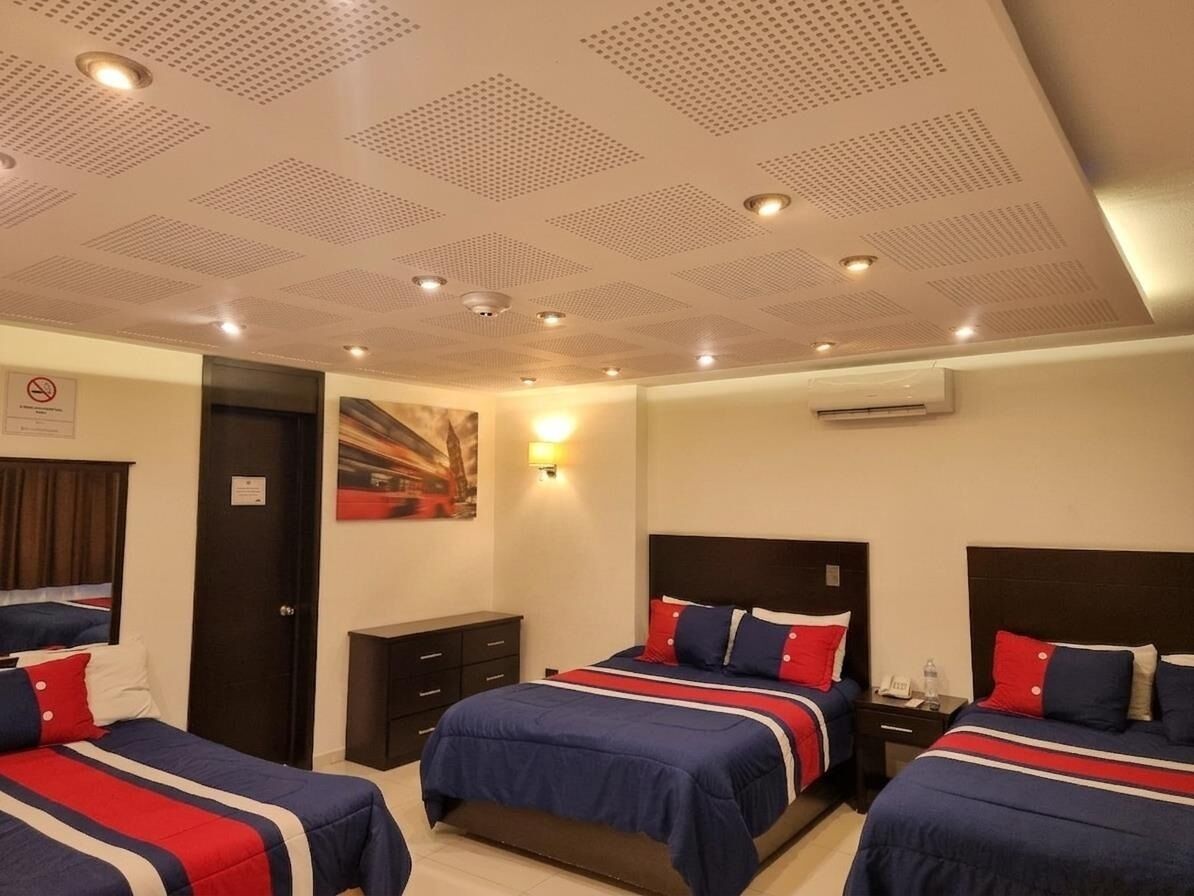 Ein Hotelzimmer mit drei Betten, einer Decke mit eingelassener Beleuchtung, einer Klimaanlage und einem Bild an der Wand.