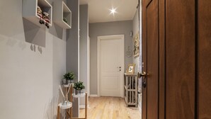 A hallway with a wooden floor, a white door, and shelves with items. - Comfortable apartment located on two levels, located on the ground floor of a building. Shared entrance with another apartment under our management.In 90 m2 of space it comfortably accommodates two people with a double bedroom located on the upper floor. (Roma)