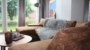 Een gezellige woonkamer met een bruine leren bank, een grijze zachte plaid en een tafel met een decoratieve vaas en een fruitschaal.