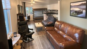 A compact living space with a leather sofa, a bunk bed, a small table, and a television. - Chalet Rustique sur île (Saguenay)
