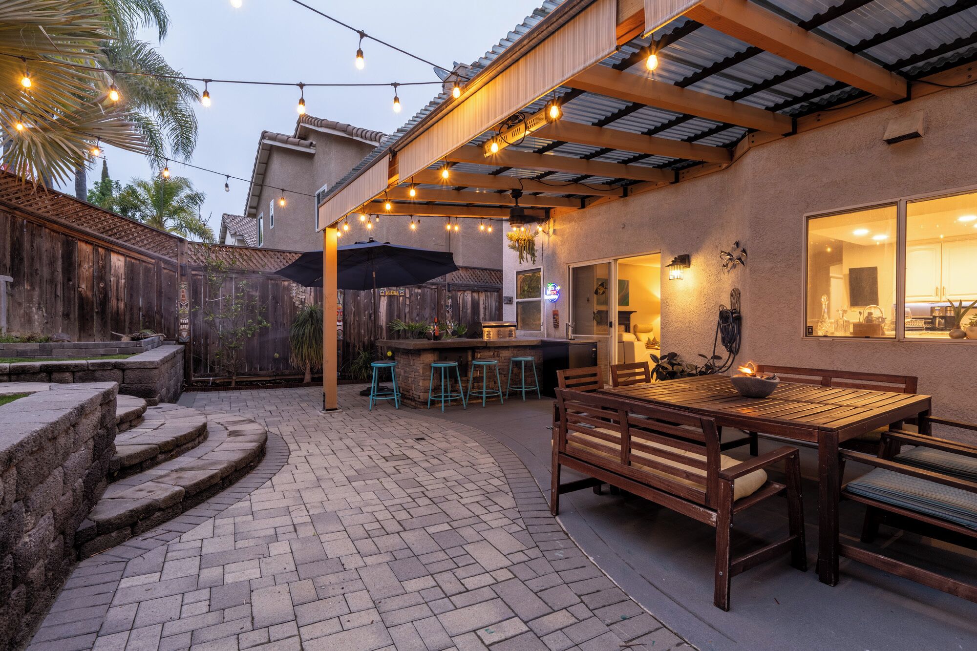 A patio area with a wooden table and chairs, a bar counter, and string lights.