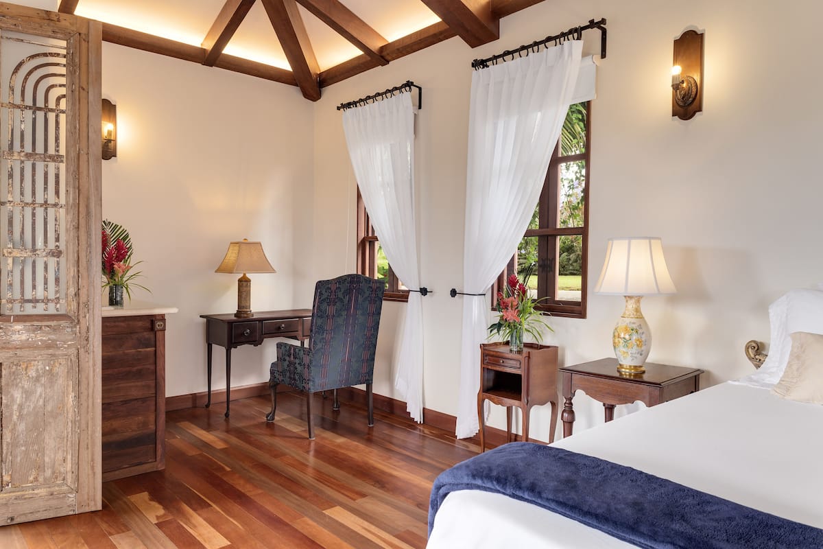 A bedroom with a bed, desk, chair, and a window with curtains.