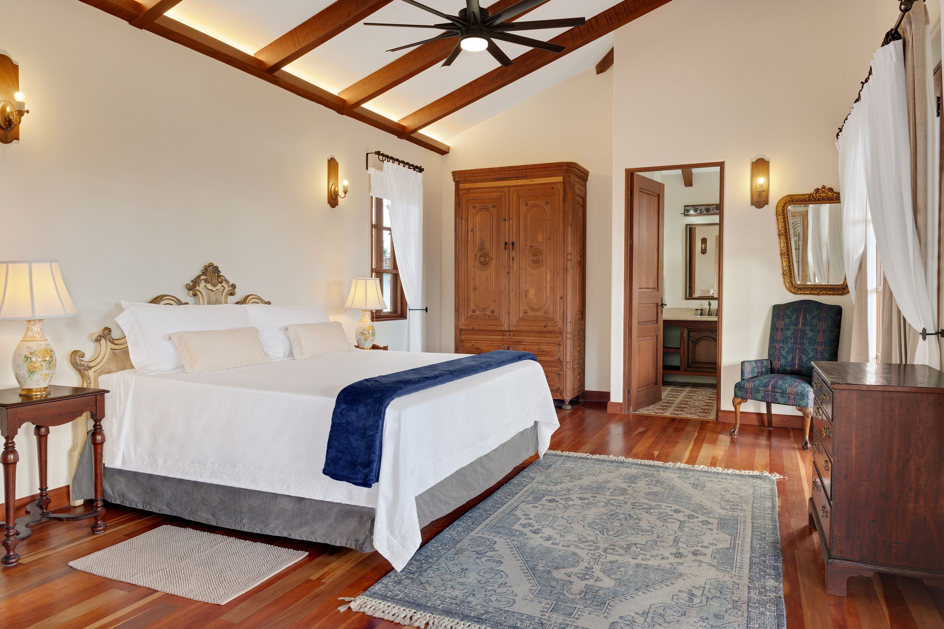 Un dormitorio con cama, armario de madera, silla y espejo.