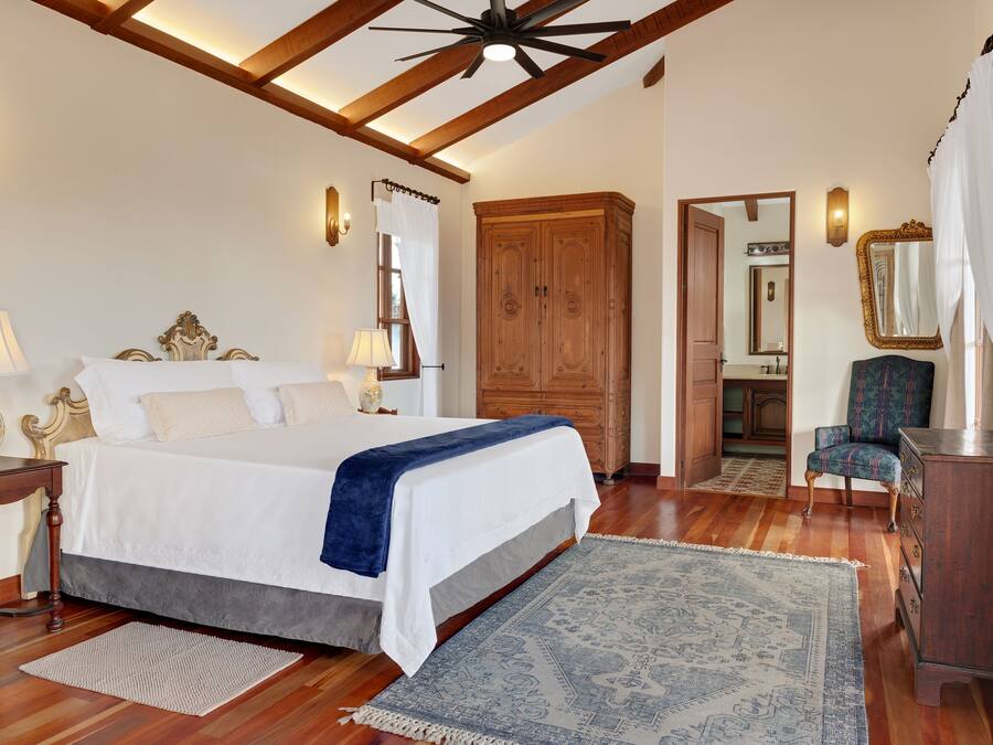 Un dormitorio con cama, armario de madera, silla y espejo.