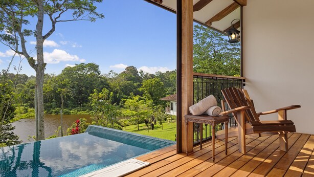 Una terraza de madera con piscina, una silla de descanso y vistas a un lago y follaje.