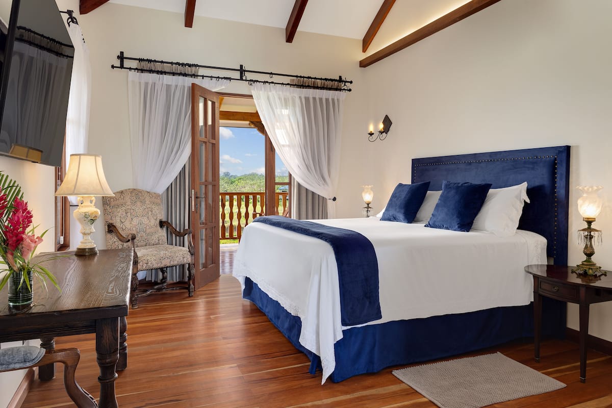 A bedroom with a large bed, a chair, a table, and a view of the outdoors.