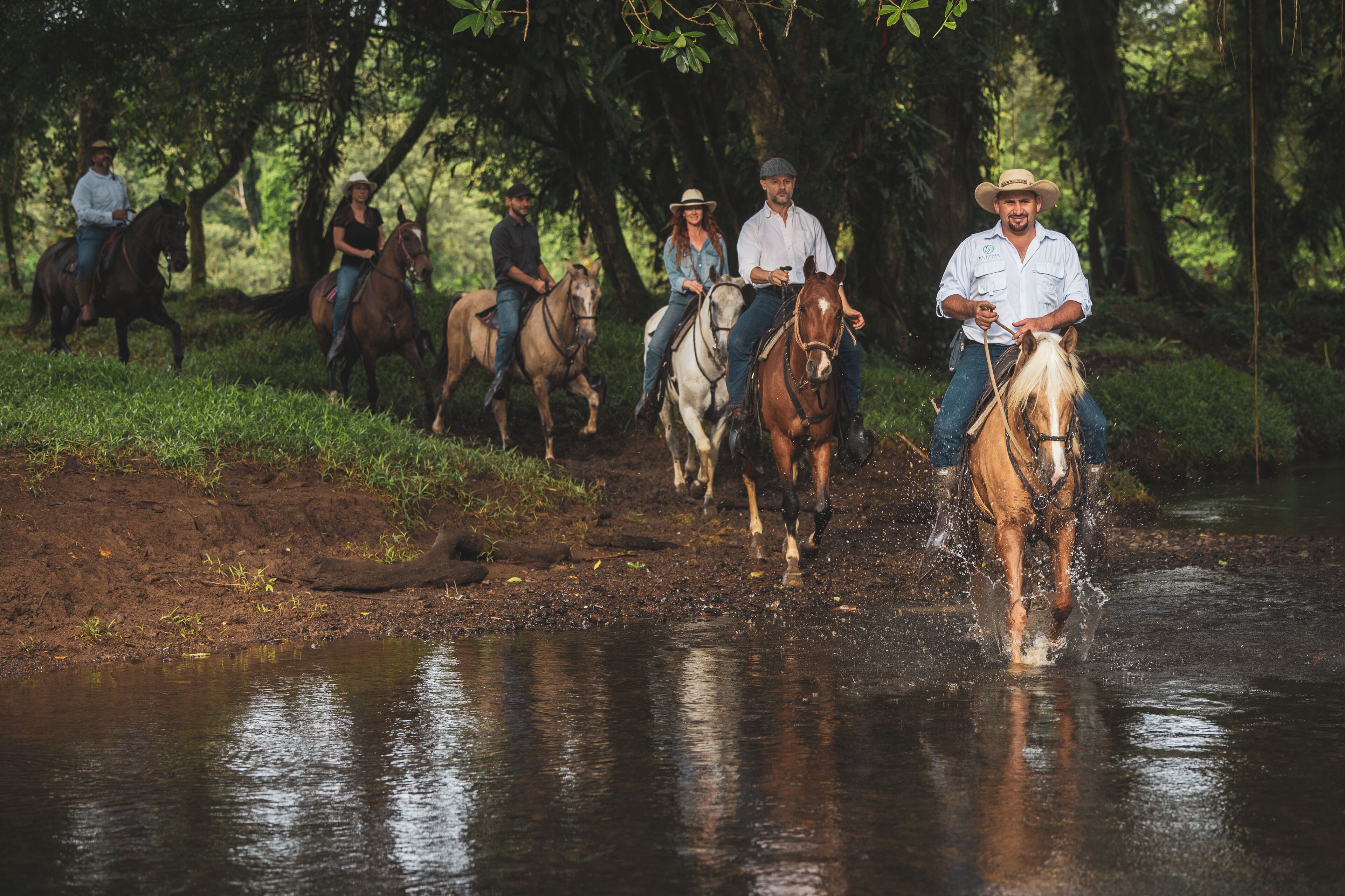 A group of people riding horses along a riverbank.