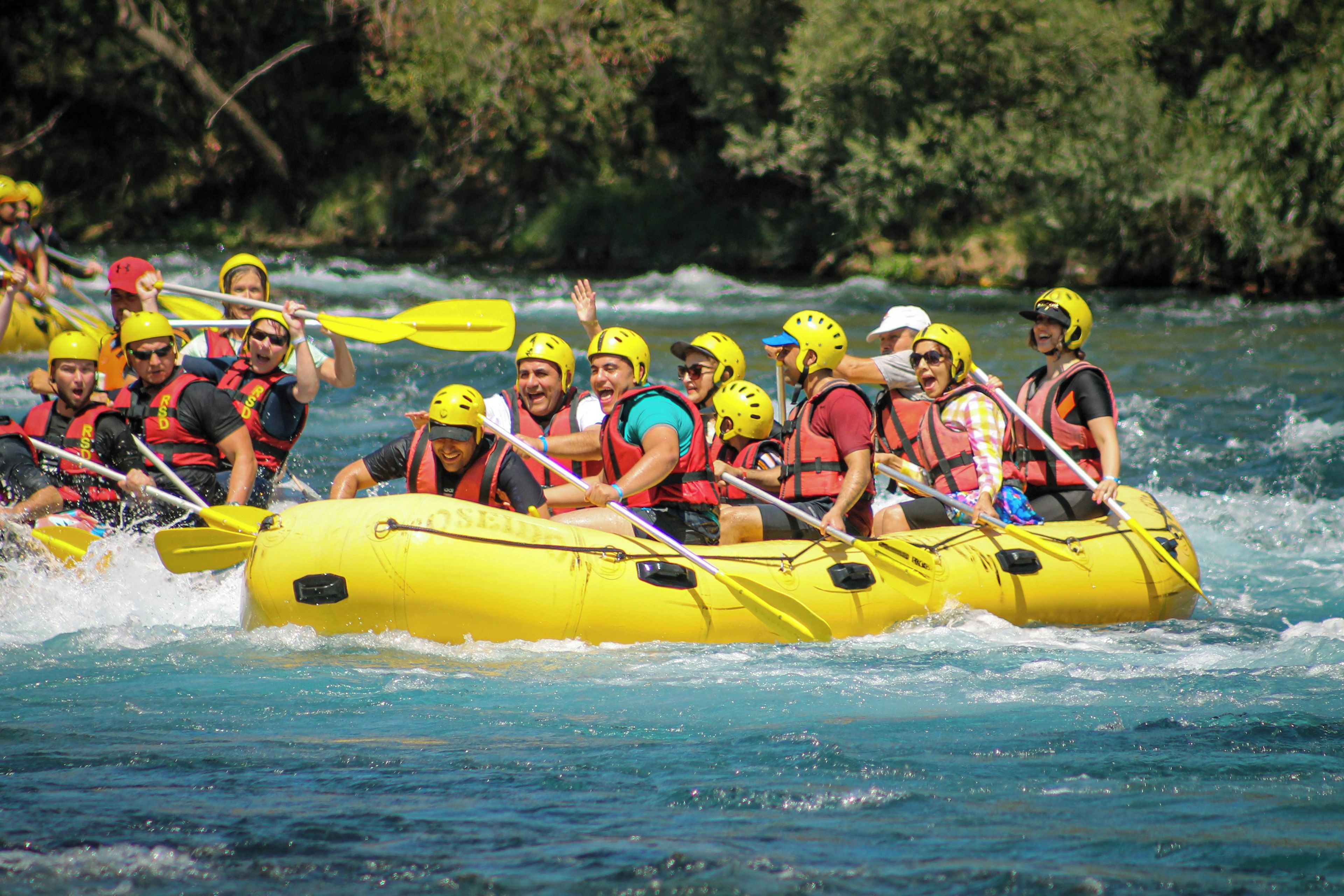 Um grupo de pessoas em um bote amarelo em um rio, usando capacetes e coletes salva-vidas.