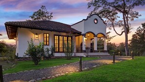 Una casa de dos pisos con techo de tejas, ventanas grandes y un porche con barandilla.