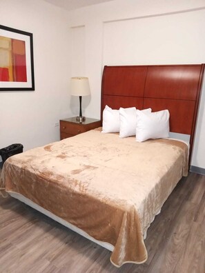 A neatly made bed with a brown bedspread, a wooden headboard, and white pillows. There is a bedside table with a lamp and a framed picture on the wall.