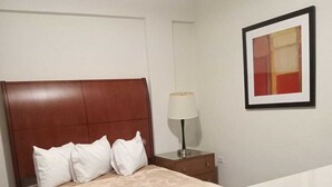 Una habitación de hotel con una cama, una mesita de noche, una lámpara y un cuadro en la pared.