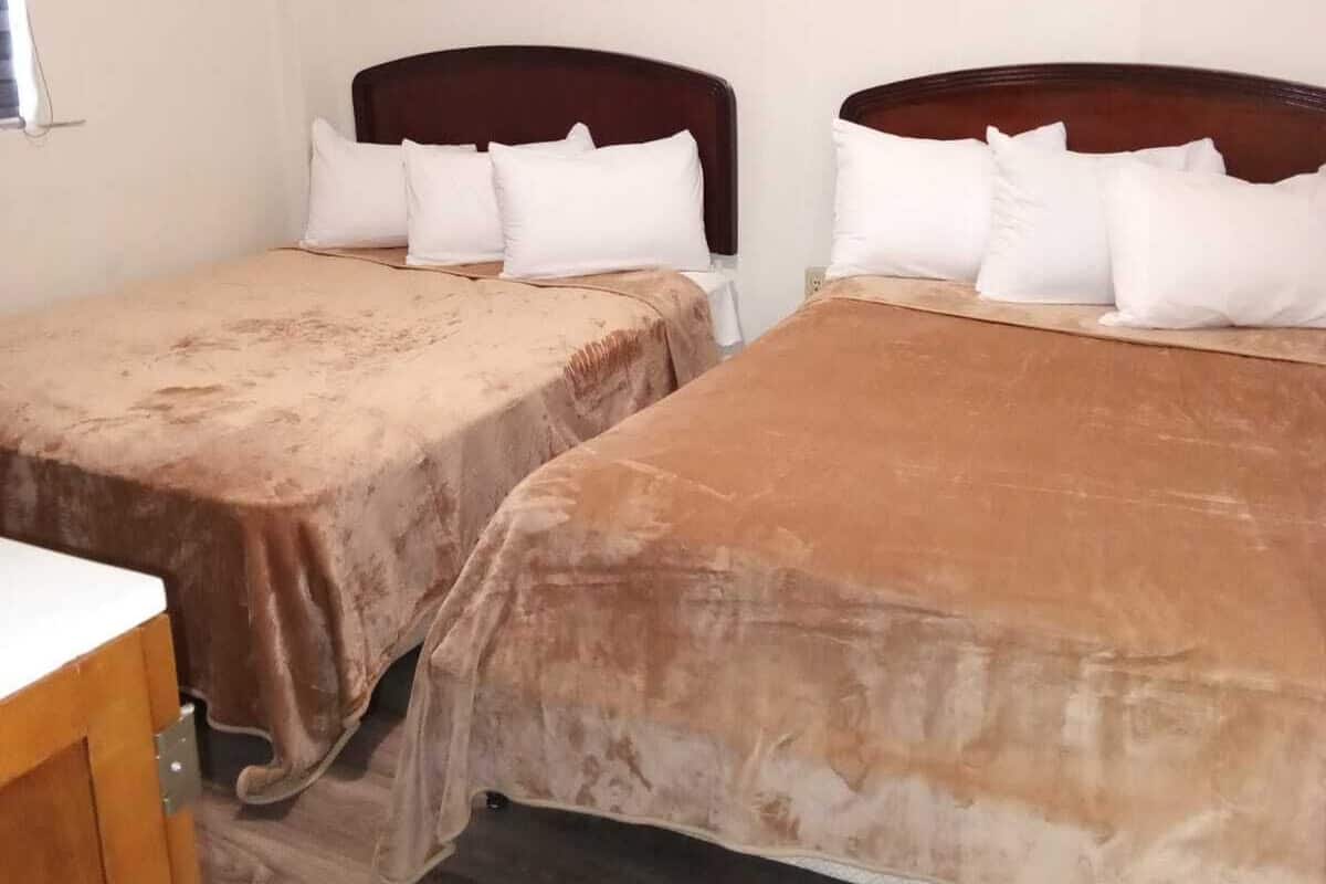 Habitación de hotel con dos camas individuales, cada una con cabecero de madera y ropa de cama blanca.