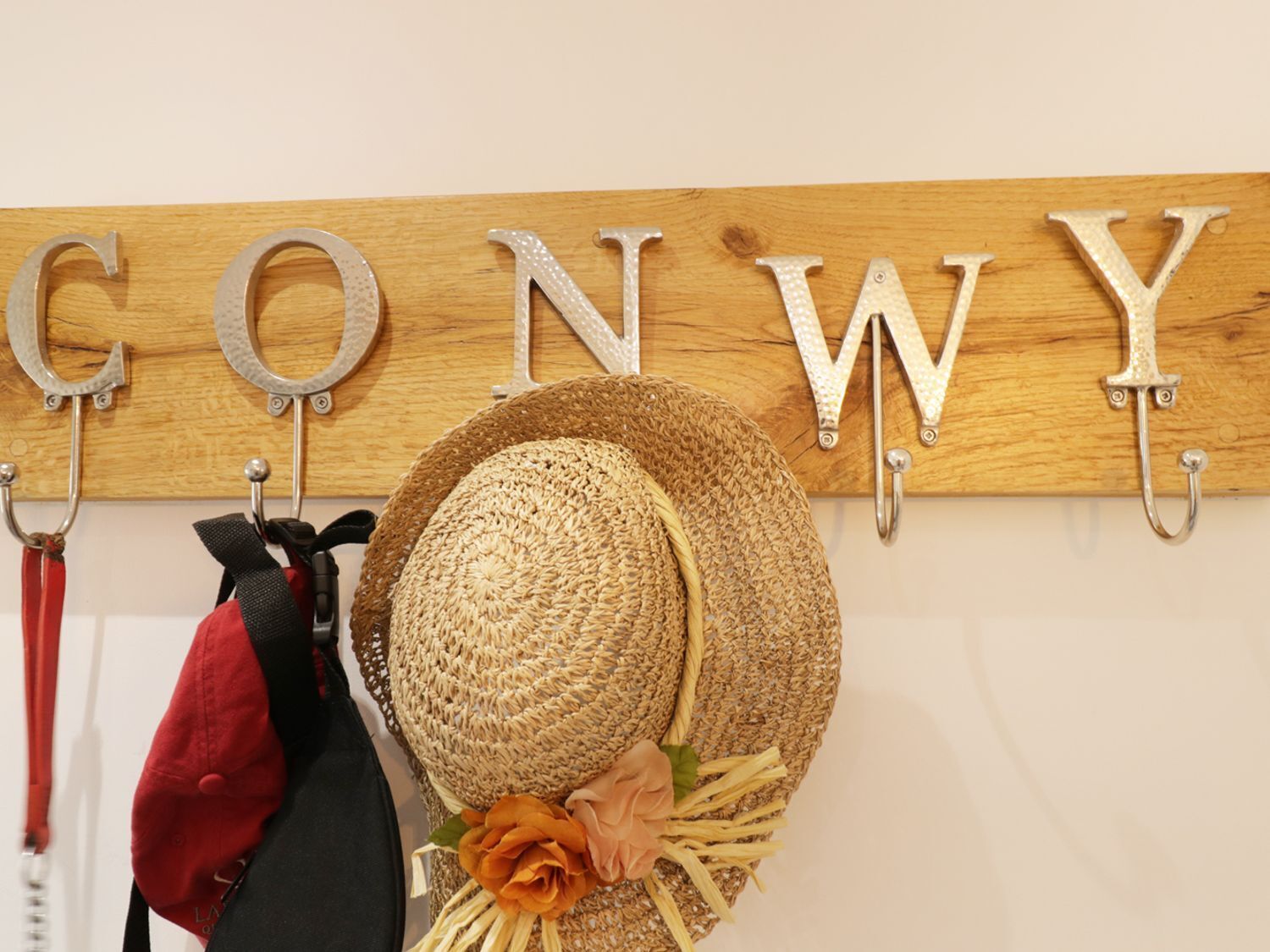Pared de madera con ganchos metálicos que sostienen un sombrero de paja y un bolso rojo.