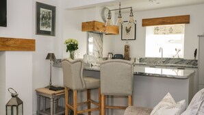 Una cucina moderna con un piano di lavoro in marmo, sgabelli da bar in legno, un lampadario e un'ampia finestra.