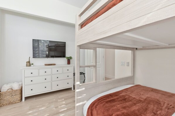 A modern bedroom with a bunk bed, a white dresser, a flat-screen TV, and a large mirror.