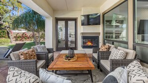 An outdoor seating area with wicker furniture, a wooden table, and a fireplace. - Serenity Retreat at Montage, by GPM - Pool + Gameroom + More! Walk to Festivals (Indio)