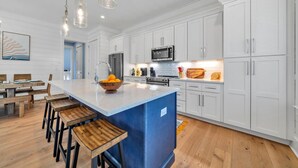 Una cucina moderna con mobili bianchi, un'isola blu, sgabelli di legno e illuminazione a sospensione.