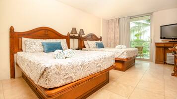 A hotel room with two wooden beds, a television, and a balcony with a view of palm trees.