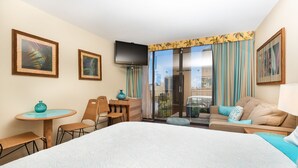 A hotel room with a large bed, a desk with a chair, a small table with a vase, a sofa with cushions, a TV mounted on the wall, and a sliding glass door leading to a balcony with a city view. - *Free Parking*Beautiful Views*10 Min to Beach* (Honolulu)