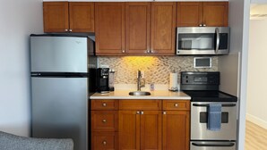 A compact kitchen with wooden cabinets, a stainless steel refrigerator, a microwave, a coffee maker, and a stove.