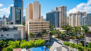 A high-rise hotel with multiple floors, a swimming pool, and palm trees in the foreground.