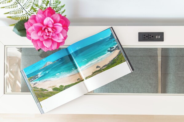 A book with a beach scene on the cover, placed on a white surface with a power outlet nearby.