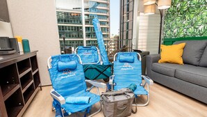A hotel room with a seating area featuring blue striped chairs, a grey sofa with a yellow pillow, and a grey bag on the floor.