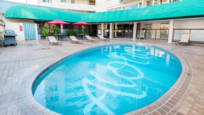 Una piscina con borde de azulejos y un toldo verde.