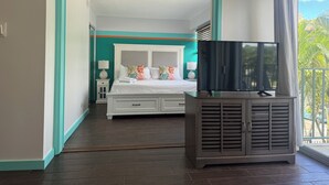 Un dormitorio con cama, mesitas de noche, un televisor en un mueble y un balcón con vistas.