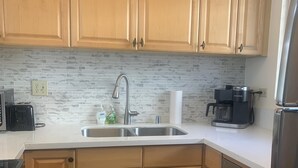 Una cocina con armarios de madera, un lavamanos de acero inoxidable, una cafetera y un lavavajillas.
