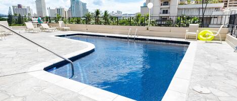 Una piscina en la azotea con sillones de descanso y vista al horizonte de la ciudad.