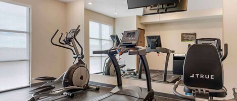 Un gimnasio con cintas de correr, elíptica y bicicleta estática.
