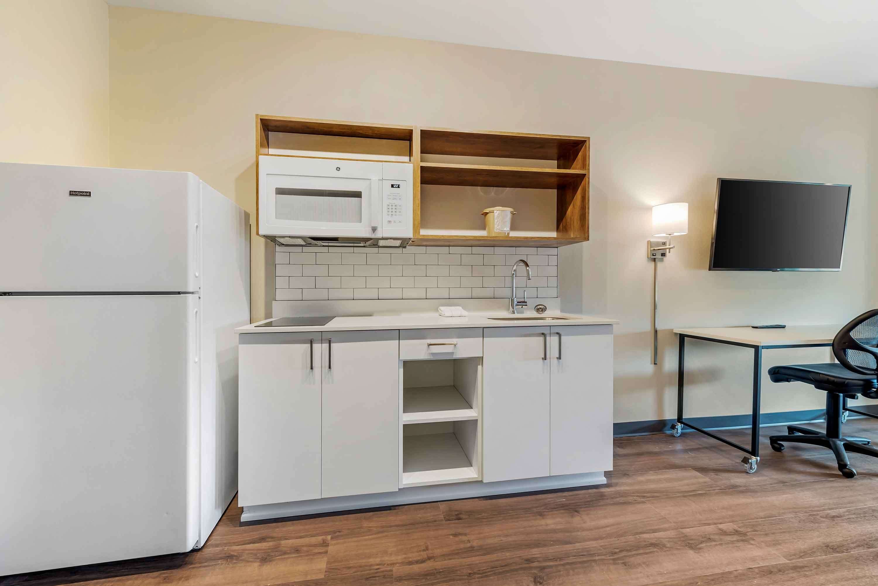 Une cuisine compacte équipée d’un réfrigérateur, d’un four à micro-ondes et d’étagères en bois.