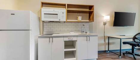 A compact kitchen with a refrigerator, microwave, and wooden shelves.