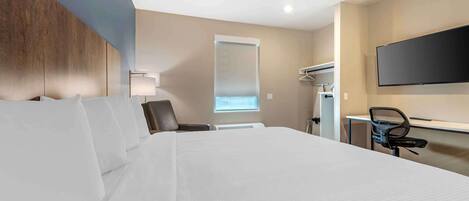 A hotel room with a large bed, a desk with a chair, a flat-screen TV, a window, and a wall-mounted air conditioning unit.