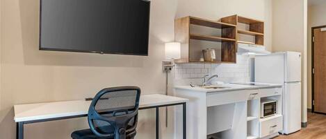 A modern kitchen with a flat-screen TV, a white countertop, and a wooden shelf unit.