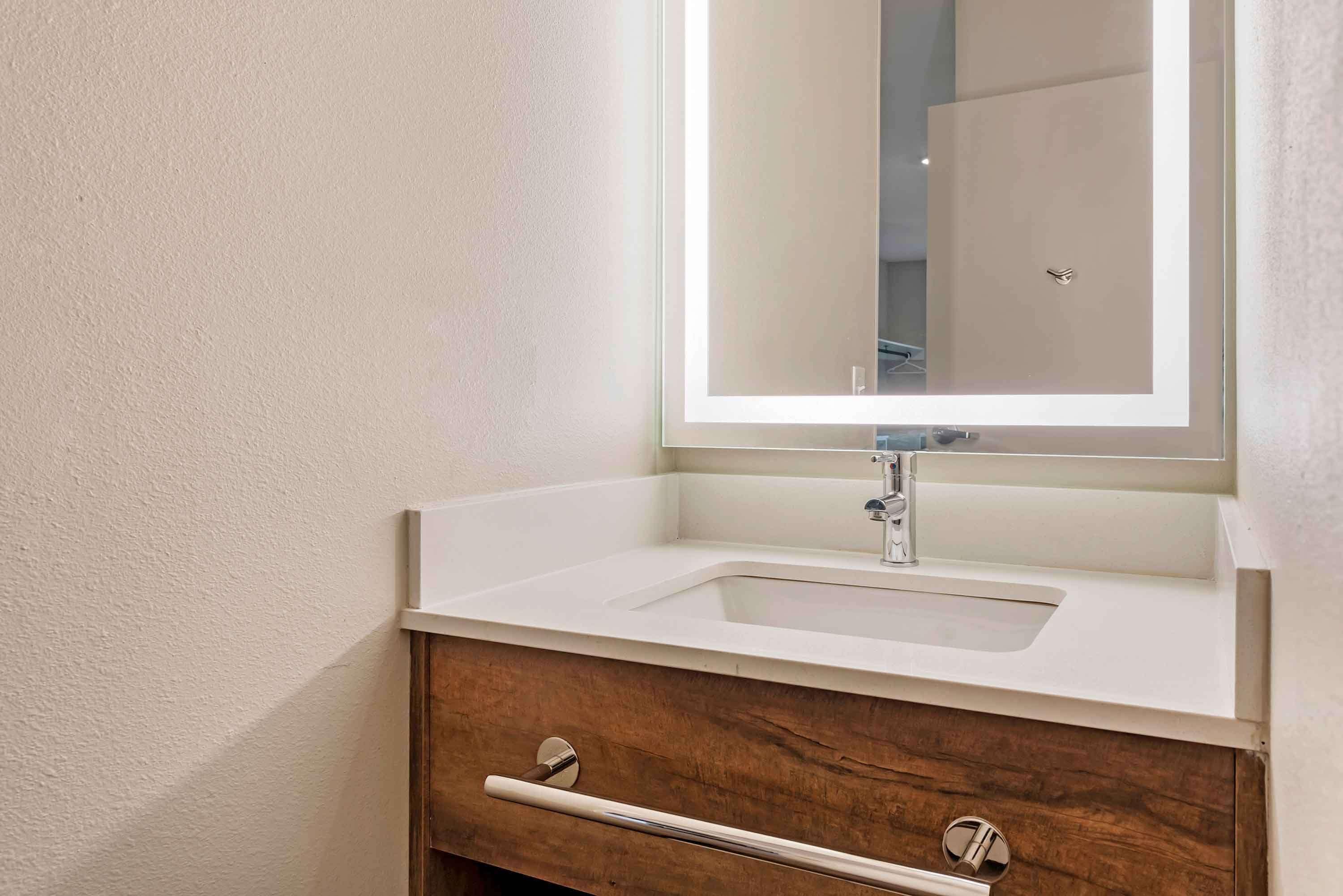Een badkamer met een wit wastafel, een spiegel met verlichting en houten kastjes.