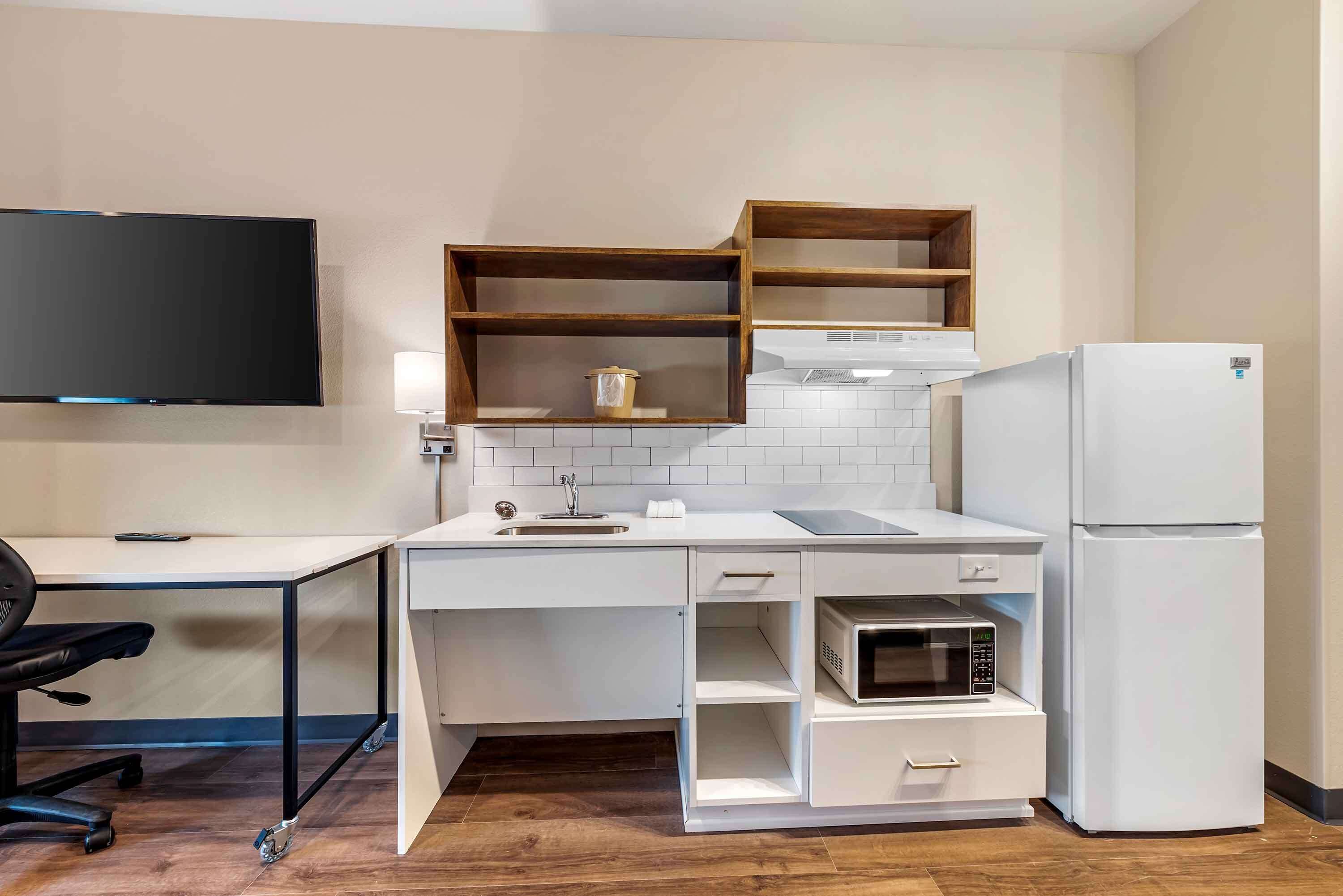 Une cuisine compacte équipée d’un four à micro-ondes, d’un réfrigérateur et d’étagères en bois au-dessus du plan de travail.