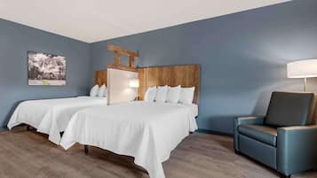 A hotel room with two beds, a wooden headboard, a blue armchair, and a painting on the wall.