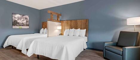 A hotel room with two beds, a wooden headboard, a blue armchair, and a painting on the wall.