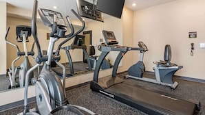 Un gimnasio con varios equipos de ejercicio, incluyendo cintas de correr y bicicletas estáticas, y un espejo grande que refleja el espacio.