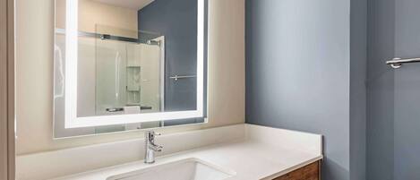 Un baño con un lavabo blanco, un espejo con luz y una puerta.