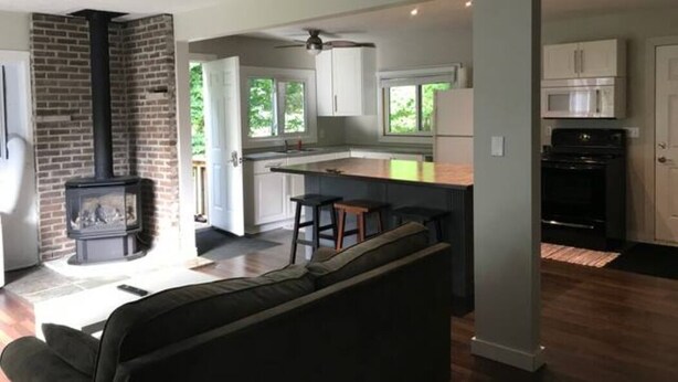A modern kitchen with a central island, a built-in stove, and a dining area with a bar. - Point Clark Cottage Getaway (Huron Kinloss)
