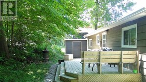 A wooden deck with a bench, a covered area, and a gravel path leading to a house with a garage. - Point Clark Cottage Getaway (Huron Kinloss)