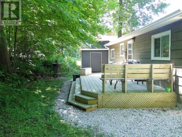 A wooden deck with a bench, a covered area, and a gravel path leading to a house with a garage.