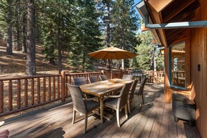 A wooden deck with a table and chairs, surrounded by a wooden railing, overlooking a forested area.