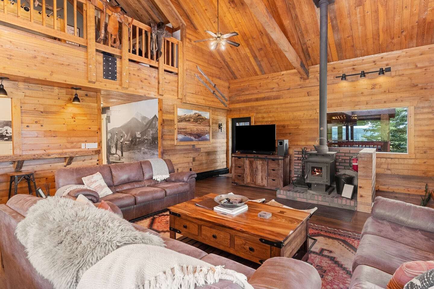 A cozy log cabin interior with a wooden ceiling, a fireplace, a television, and a sofa.